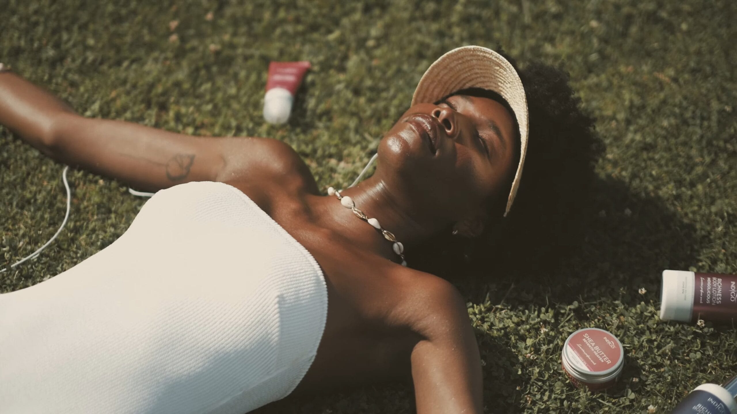 Kobieta relaksuje się na trawie, głowa w promieniach słońca, wokół niej kosmetyki Indigo Nails.