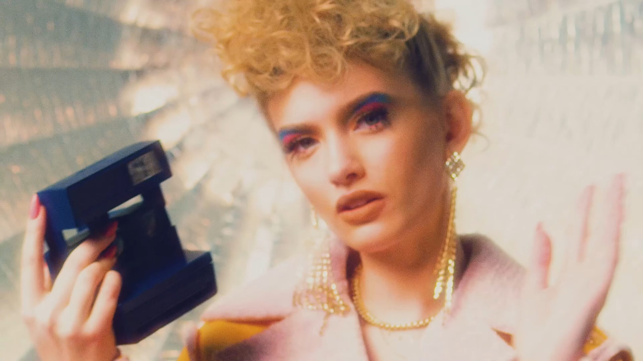 Kobieta z złotym naszyjnikiem trzyma niebieski aparat fotograficzny w ręku, uśmiechając się do obiektywu.