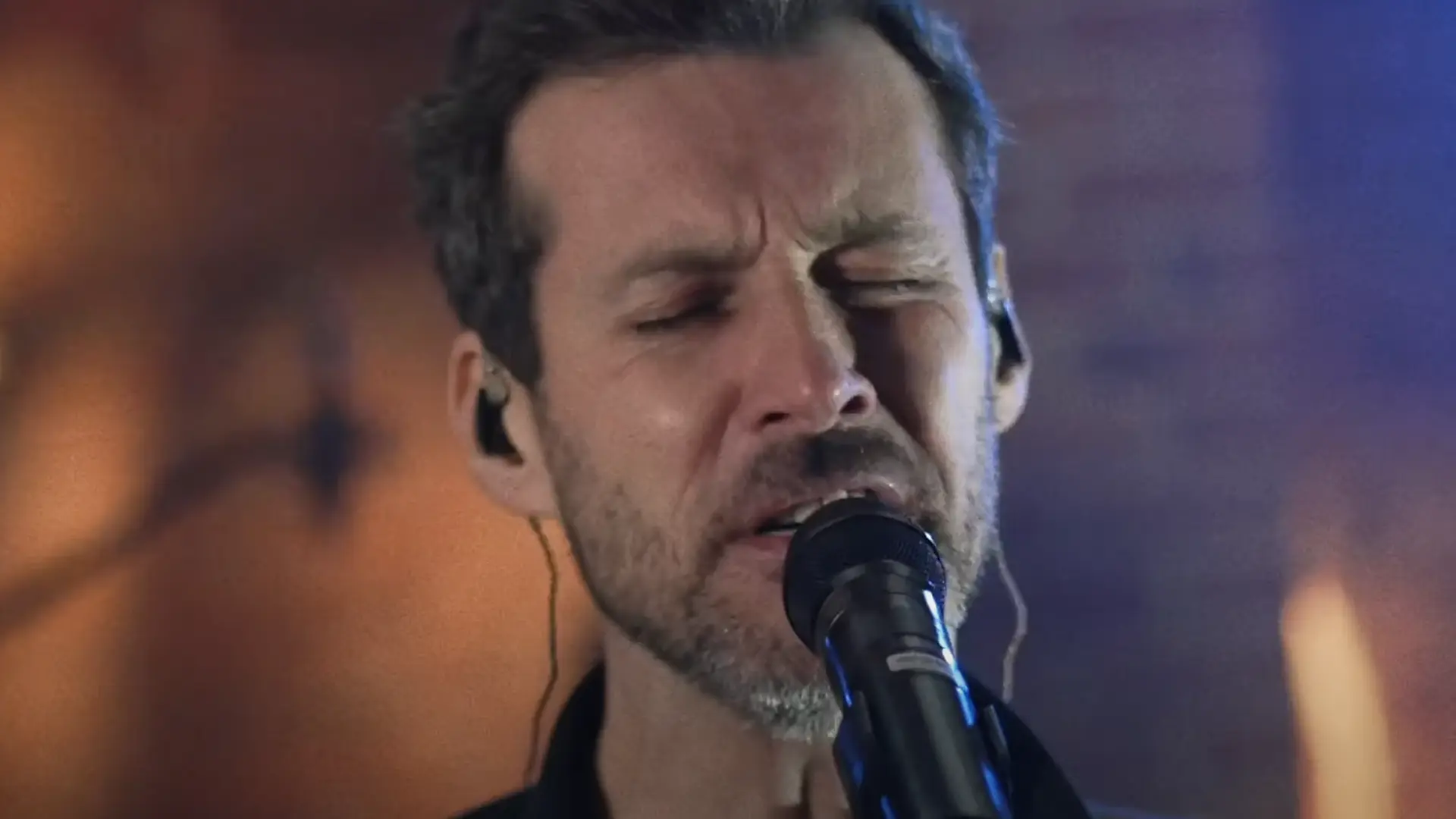 Mężczyzna z zamkniętymi oczami, śpiewający do mikrofonu, oddaje się pasji muzycznej.