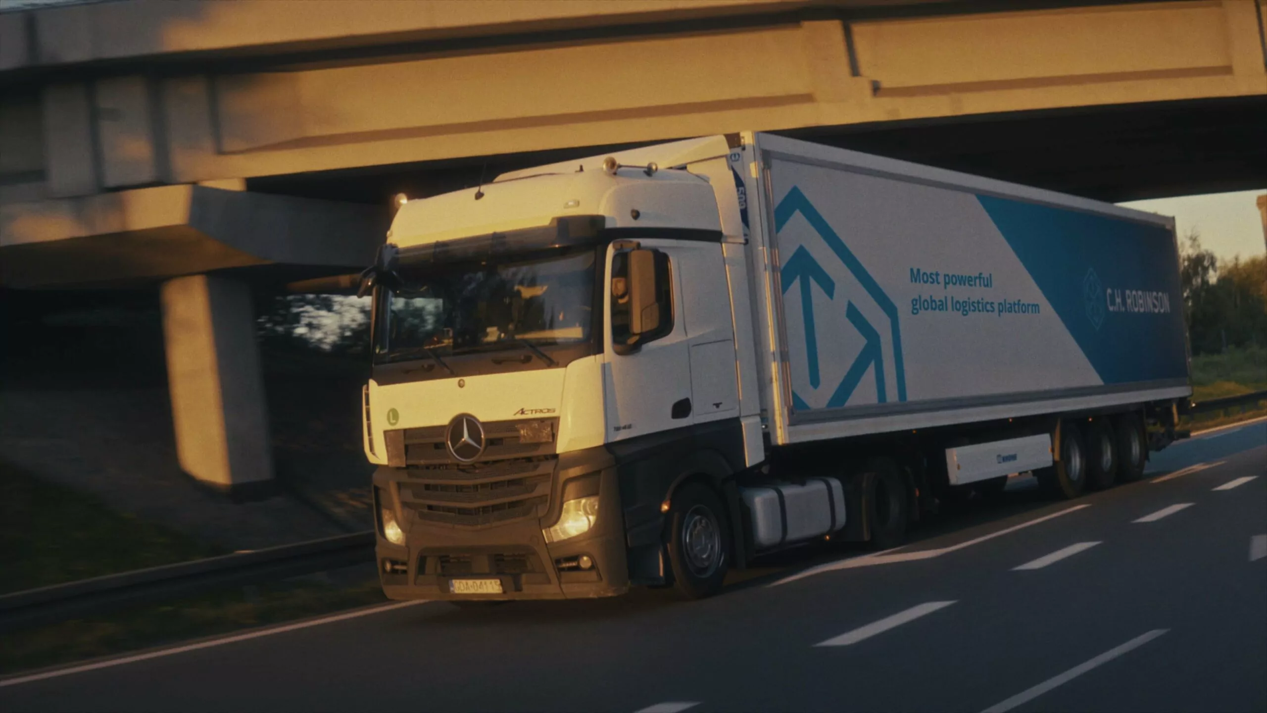 Ciężarówka C.H. Robinson na autostradzie, przejeżdżająca pod wiaduktem, w słoneczny dzień.