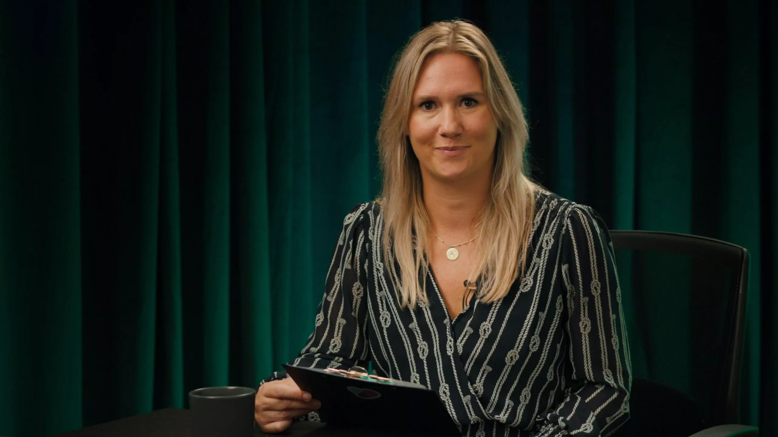 Osoba przy stole z kawą, prowadząca podcast, trzymająca notatki w ręku.