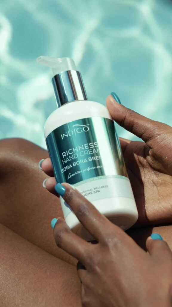Dłonie kobiety trzymają butelkę kremu do rąk Bora Bora Breeze Shimmer przy basenie, w otoczeniu letniego słońca.