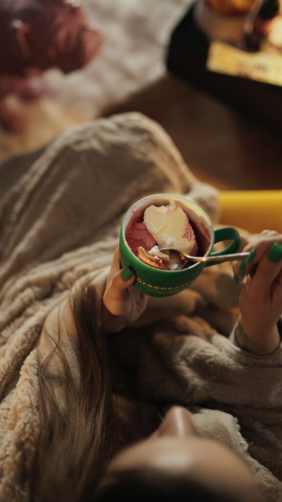 Kobieta delektuje się lodami z zielonego kubka Greensetter od Indigo Nails, wyrażając radość z posiłku.