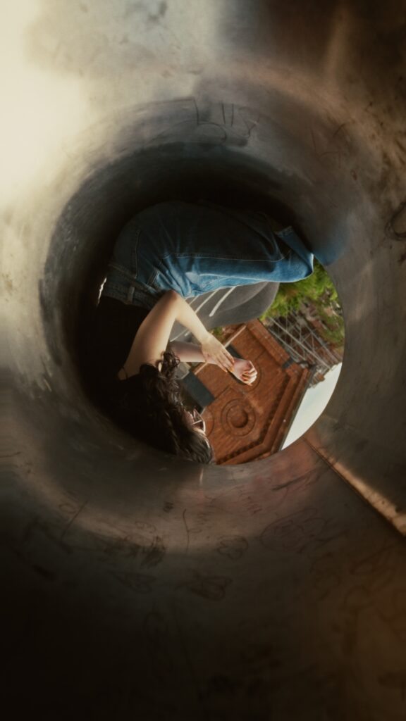 Siedząca postać wewnątrz metalowej rury, otoczona gładką, stalową powierzchnią.